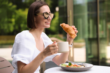 Wall Mural - Happy woman having tasty breakfast in outdoor cafe