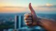 © sarana - Thumbs Up Hand Gesture: A hand giving a thumbs-up with a blurred cityscape in the background.