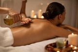 Massage therapist pouring oil on lady back at luxury spa decorated with candles, body care concept. Woman enjoying relaxing massage with aromatherapy