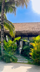 Wall Mural - Tropical vacation concept: idyllic thatched-roof bungalow surrounded by lush greenery on a sunny day, perfect for summer getaways