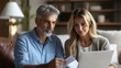 © Neural Pixels - Couple collaborates on paperwork while working on a laptop in their cozy living room