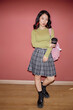 © Seventyfour - Vertical full shot of confident young Asian female student wearing plaid skirt in preppy style holding reusable coffee cup against pinkish red wall, copy space