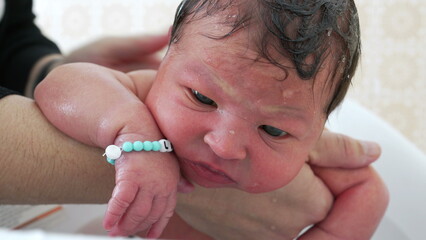 Bathing newborn baby infant inside bathtub during first week of life. relaxed child enjoying first bath, mother's hand rubbing baby's hair and body