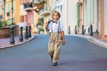 Wall Mural - Smart casual children in suits, ties and bows,  walking on a narrow street with houses in Monaco-Ville, Monaco. Business clothing, teenagers, preschool boy and mother