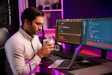 Smart IT developer drinking coffee cup while working in software development coding on pc screen, presenting program application update online website database at neon lighting cyber office. Surmise.