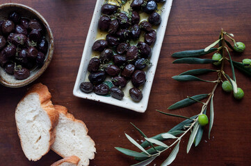 Top view  image of black olives with olive oil and sprinkled fresh thyme in two different ceramic dishes with Turlish bread and olive branch on wooden table