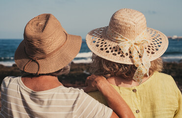 Sticker - Rear view of a couple of women, one elderly and one middle-aged wearing hats while enjoying a sunny day at the beach looking at the horizon. Summer vibes