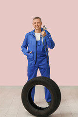 Wall Mural - Portrait of male auto mechanic with tire and wrenches on pink background