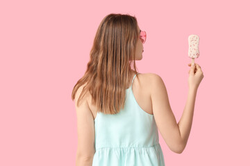 Wall Mural - Young woman holding white chocolate covered ice cream with strawberry on pink background