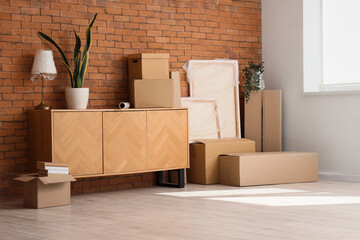 Poster - Furniture, houseplant and cardboard boxes with belongings near brown brick wall. Moving house concept