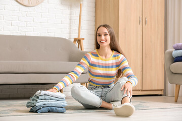 Poster - Young woman with stack of jeans sitting on floor at home