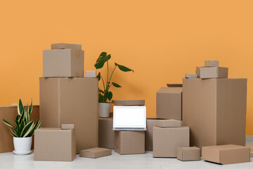 Wall Mural - Blank laptop with moving boxes and plants near orange wall in room