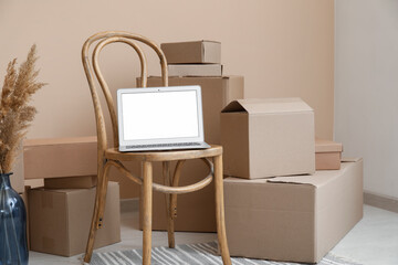 Canvas Print - Blank laptop on chair with moving boxes near beige wall in room