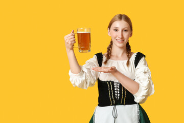 Beautiful happy Octoberfest waitress pointing at  mug of beer on yellow background