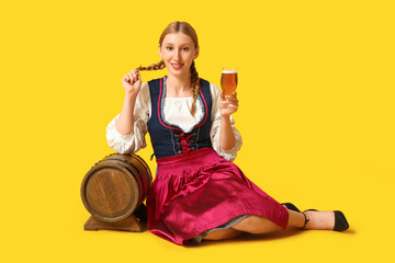 Beautiful happy Octoberfest waitress with barrel and glass of beer sitting on yellow background