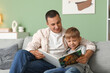 © Pixel-Shot - Happy father with his little son reading book on sofa at home