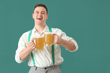 Wall Mural - Handsome young happy man in traditional German clothes with mugs of beer on green background