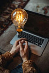 Poster - A person sits at a table with a laptop and a light bulb, focusing on their work