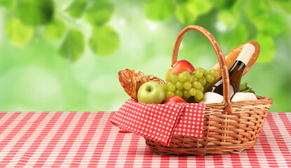 Wall Mural - Picnic basket with foods and wine on table in nature. Space for text