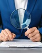 © ParinApril - business professional examining documents with a magnifying glass, symbolizing careful analysis and attention to detail.