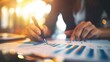© SSTC AI Photo&Video - Close-up of a person analyzing financial charts and graphs with a pen and a laptop, highlighting data analysis, financial planning, and business strategy..