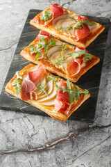 Wall Mural - Delicious baked puff pastries with pear, cream cheese, jamon and arugula close-up on marble board on table. Vertical