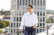 © sofiko14 - Confident woman standing on rooftop in urban setting looking away. Casual outfit with white shirt and jeans. Daytime image with city buildings in background. Concept of confidence, aspirations.