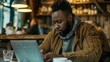 © Ameer - African American male freelancer working remotely on a laptop in a modern cafe, focused on business tasks in a casual urban setting.