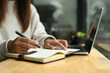 © Prathankarnpap - Cropped shot of young woman taking notes on notebook and using laptop at a coffee shop
