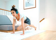 © tai - pretty woman exercise wearing headphones indoors in living room. home fitness beautiful woman exercising listening song with headset. beautiful exerciser workout wearing headphones doing fitness pose
