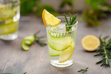 Wall Mural - Refreshing water with lemon, cucumber and rosemary in a glass on the table.