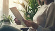 © VK Studio - Person holding a tablet in front of a large window with ample sunlight and green plants, creating a calm environment.