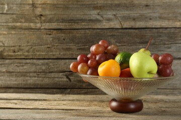 Wall Mural - Glass vase with different fresh fruits on wooden table, space for text