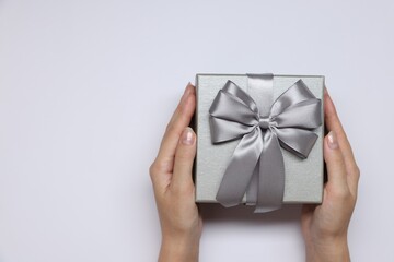 Poster - Woman holding gift box with bow on white background, top view. Space for text