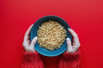 Creative image of female hands knitting instant noodles in a blue bowl.