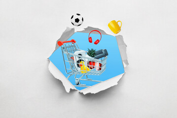 Poster - Ragged hole in paper with a shopping cart full of products emerging. Concept of shopping and buying various items through a creative perspectiv