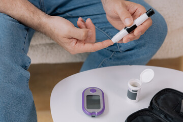 Diabetic senior man on wheelchair checking blood sugar level with fingerstick testing glucose meter. Elderly man with type 1 diabetes using blood glucose monitor at home.