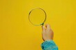 © SY - Hand holds magnifying glass against yellow background. Conceptual image for searching, discovery, or finding something.