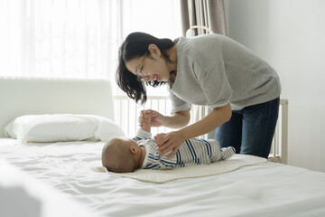 Asian Mother playing with baby on bed in a bright bedroom. Natural light indoor lifestyle photography. Parenting and bonding concept