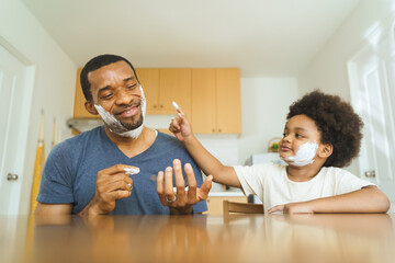 Wall Mural - Black African American Father and young son playfully applying shaving cream to faces in a kitchen setting. Indoor candid photography. Family bonding