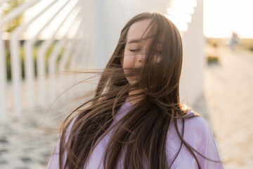 Portrait of a happy teenage girl with long hair walking in the city at sunset in summer