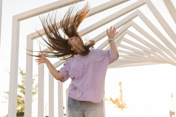 Portrait of a happy teenage girl with long hair walking in the city at sunset in summer