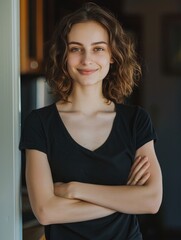 Wall Mural - A woman with a black shirt and brown hair is smiling and posing for a picture. She is wearing a black shirt and has her arms crossed