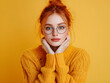 © Marcos - Vibrant Red-Haired Woman in Messy Bun Against Bright Yellow Background, Wearing Fashionable Round Glasses and Cozy Oversized Yellow Sweater, Exuding Warmth, Joy, and Approachability in Cheerful