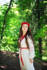 Wall Mural - Young beautiful woman in Slavic traditional clothing stands in a serene forest