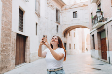 Wall Mural - Happy female Tourist taking photos of a historic building in the old town of a European city. A young woman takes pictures of beautiful views of the city on her phone. Travel Explore Europe.