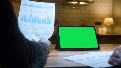 Two unknown men working with tablet computer with green mock up screen on table in the kitchen. Co-workers working with papers, remote work, home office concept	