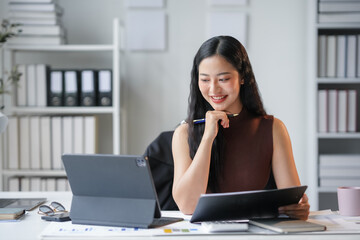 Asian businesswoman is smiling while working on documents at her desk in her bright and modern office