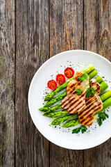 Sticker - Pork loin steaks and cooked green asparagus served on white plate on wooden table
