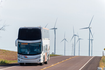 Double-decker bus on rural road with wind turbines showcasing renewable energy.